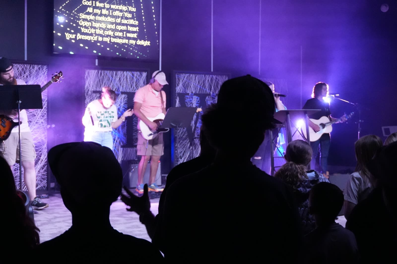 The worship band on stage under purple light, seen from the crowd at CrossOver